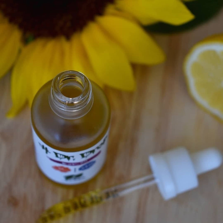 Open Dr Drop bottle with dropper on wood beside sunflower and lemon slice showing golden oil texture