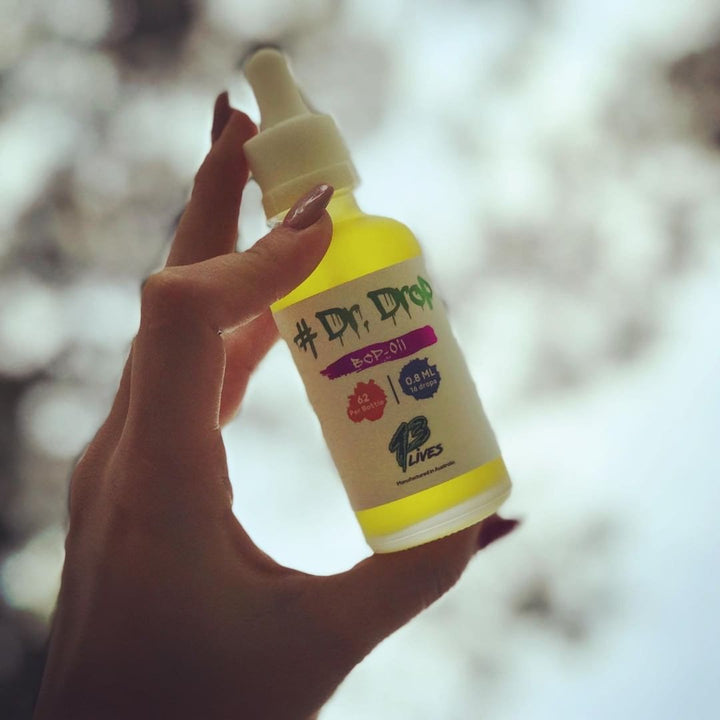 Person holding 13Lives Dr Drop BCP + Myrcene Oil bottle up to light showing golden hue and label details