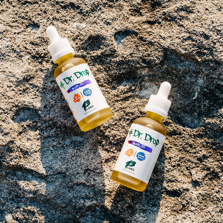 Two bottles of 13Lives Dr Drop BCP + Myrcene Oil with white labels and droppers lying on a sunlit rock surface