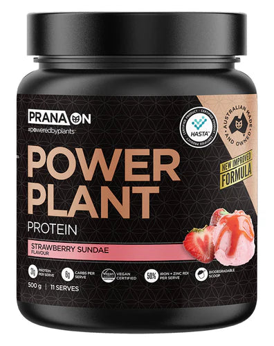 A container of Prana On Power Plant Protein powder in Strawberry Sundae flavor. The packaging is black with gold and white text and an image of a chocolate bar.